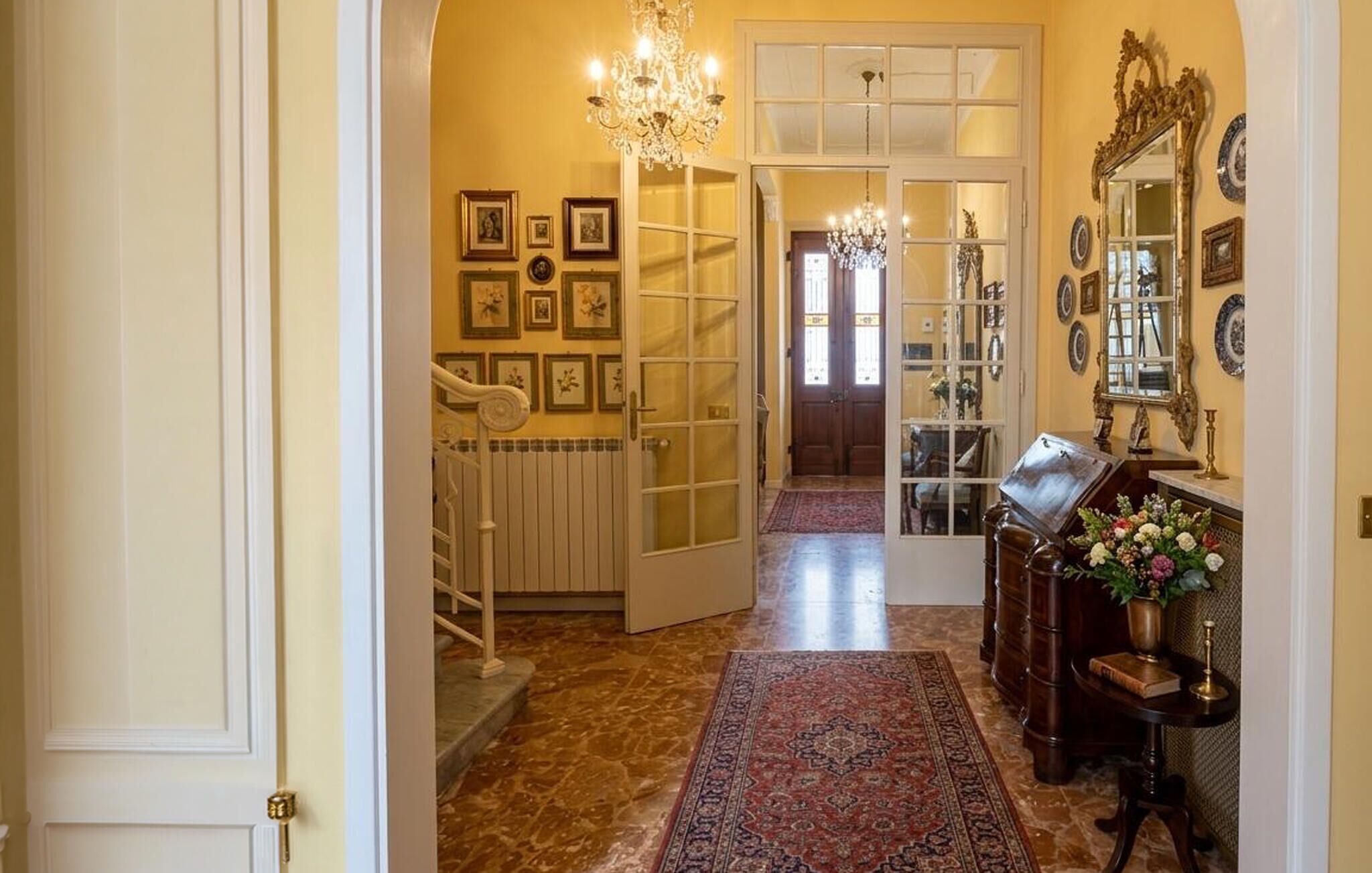 Ein Flur mit einem Chandelier, gerahmten Bildern, einem Holzschrank und einem Spiegel.