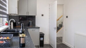 Une petite cuisine équipée d’un évier, d’une machine à café et d’une bouteille de vin posée sur le plan de travail.