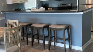 A kitchen with white cabinets, a microwave, a refrigerator, and a bar area with stools. - Waterway views, beautiful sunsets, pools, hot tubs, balcony, grilling & beaches (North Myrtle Beach)