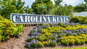 A sign with the text "CAROLINA KEYES" surrounded by a garden with purple and yellow flowers. - Waterway views, beautiful sunsets, pools, hot tubs, balcony, grilling & beaches (North Myrtle Beach)