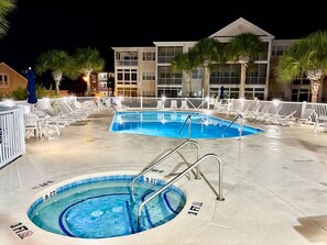 A pool area with two pools, lounge chairs, and a building in the background.