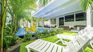 A modern outdoor patio with a swimming pool, white lounge chairs, and lush greenery. - 18 Bedroom PRIVATE HOME Jaco Beach, 5-Year of Excellence, VIP Concierge Services (Puntarenas Province)