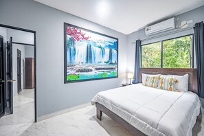 Habitació d'hotel amb un llit gran, aire condicionat fixat a la paret, una finestra amb cortines i un quadre d'una cascada.