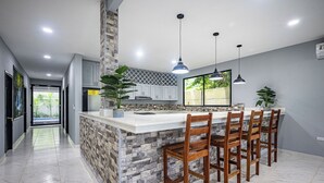 A modern kitchen with a central island, bar stools, pendant lighting, and a view to the outdoors. - 18 Bedroom PRIVATE HOME Jaco Beach, 5-Year of Excellence, VIP Concierge Services (Puntarenas Province)
