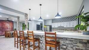 A modern kitchen with a stone backsplash, wooden bar stools, and pendant lighting. - 18 Bedroom PRIVATE HOME Jaco Beach, 5-Year of Excellence, VIP Concierge Services (Puntarenas Province)