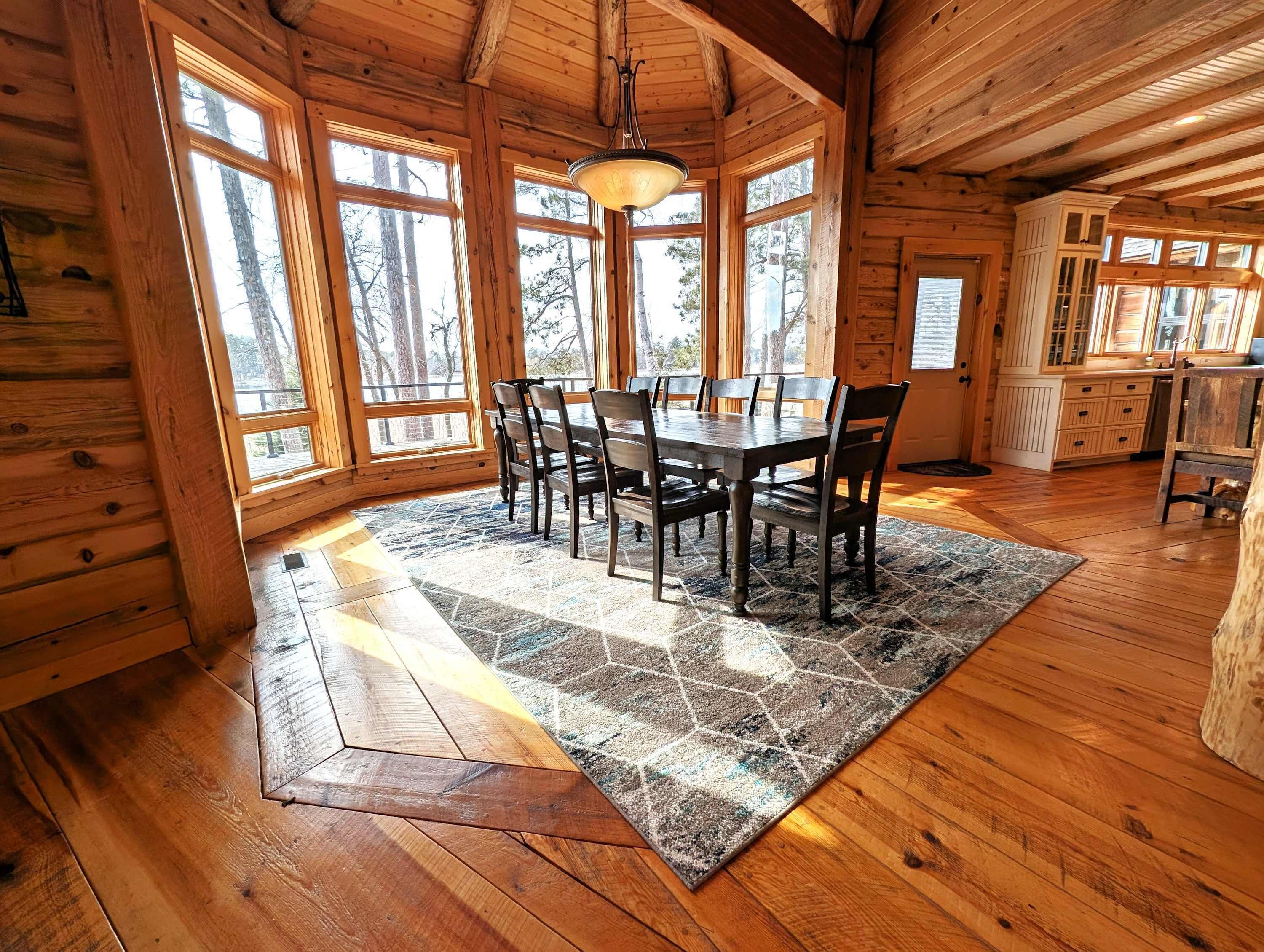 A wooden interior with a dining table and chairs, large windows, and a kitchen area.