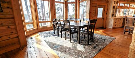 A wooden interior with a dining table and chairs, large windows, and a kitchen area.