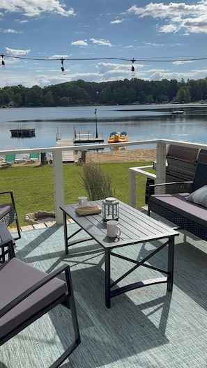Un patio con mobiliario exterior, una mesa con un farol y vistas a un lago con barcos.