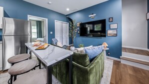 A modern kitchen with a stainless steel refrigerator, a dining table with two chairs, and a green cushioned seating area.