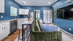 A modern kitchen with white cabinets, a stainless steel refrigerator, and a dining area with a green sofa and bar stools.