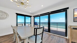 Ein Essbereich mit großem Tisch und Stühlen, großen Fenstern mit Blick auf den Strand und einer modernen Kronleuchter.