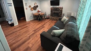 Una sala de estar con chimenea de piedra, un sofá, una mesa de comedor con sillas y un televisor montado en la pared.