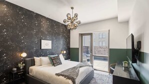 A bedroom with a large bed, a nightstand with a lamp, a dresser, and a view of the outside. - Downtown 3BR Suite Penthouse with Private Terrace Hotel (New Orleans)