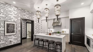 A modern kitchen with a central island, bar stools, pendant lights, and a wall with repeated text. - Downtown 3BR Suite Penthouse with Private Terrace Hotel (New Orleans)