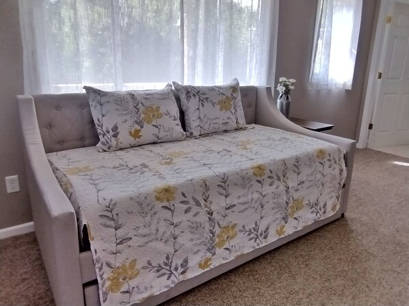 A bedroom with a bed, a window with curtains, a vase with flowers, and a door.