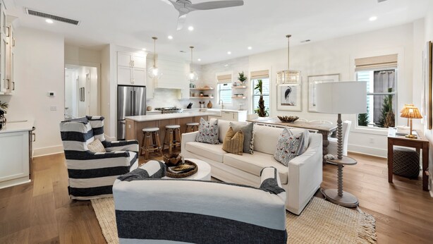 A modern kitchen with stainless steel appliances, a dining area with a white table and bar stools, and a living room with a sofa and armchairs. - Stunning Wild Dunes Home-- Fire Pit, Hot Tub, Golf Views, Walk to Marina!! (Isle Of Palms)
