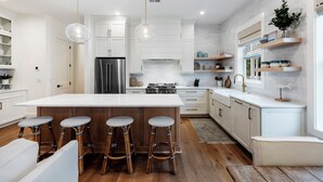 A modern kitchen with white cabinetry, a large island with stools, stainless steel appliances, and pendant lighting. - Stunning Wild Dunes Home-- Fire Pit, Hot Tub, Golf Views, Walk to Marina!! (Isle Of Palms)