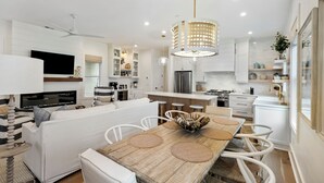 A modern kitchen with white cabinets, a central island with a wooden table, and a hanging light fixture. - Stunning Wild Dunes Home-- Fire Pit, Hot Tub, Golf Views, Walk to Marina!! (Isle Of Palms)