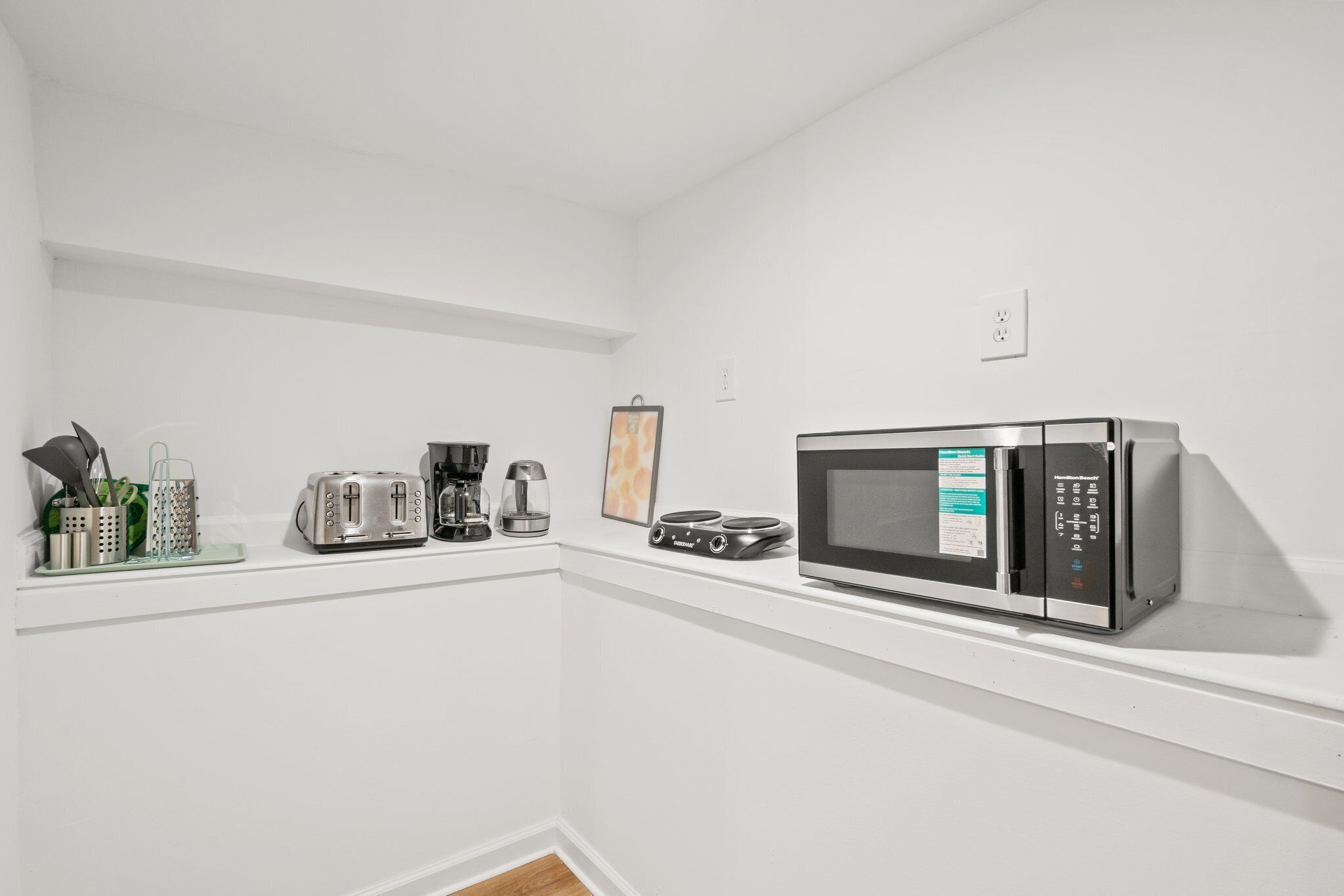 A kitchen with a microwave, toaster, coffee maker, and a small framed picture on the wall.