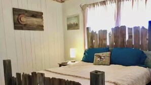 A bedroom with a wooden bed frame, a nightstand, a lamp, and a window with curtains. - Charming 2-bedroom house in Coleman with AC and WiFi.  Sleeps 6 & no pets. (Coleman)