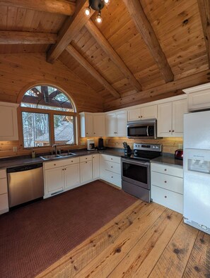 Una cocina con vigas de madera, armarios blancos, electrodomésticos de acero inoxidable y un amplio ventanal.