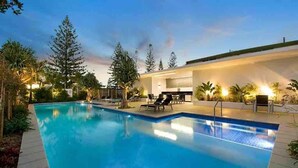 A swimming pool with lounge chairs and a modern building in the background. - Broadbeach Ocean-View Beachfront Apartment (Broadbeach)