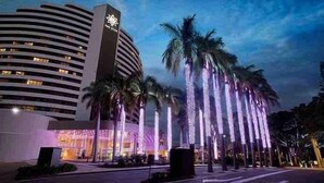 A hotel with a modern design, featuring a curved building facade and a prominent tower. Palm trees line the street in front of the hotel. - Broadbeach Ocean-View Beachfront Apartment (Broadbeach)