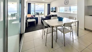 A modern living room with a dining area, large windows, and a view of the city. - Broadbeach Ocean-View Beachfront Apartment (Broadbeach)