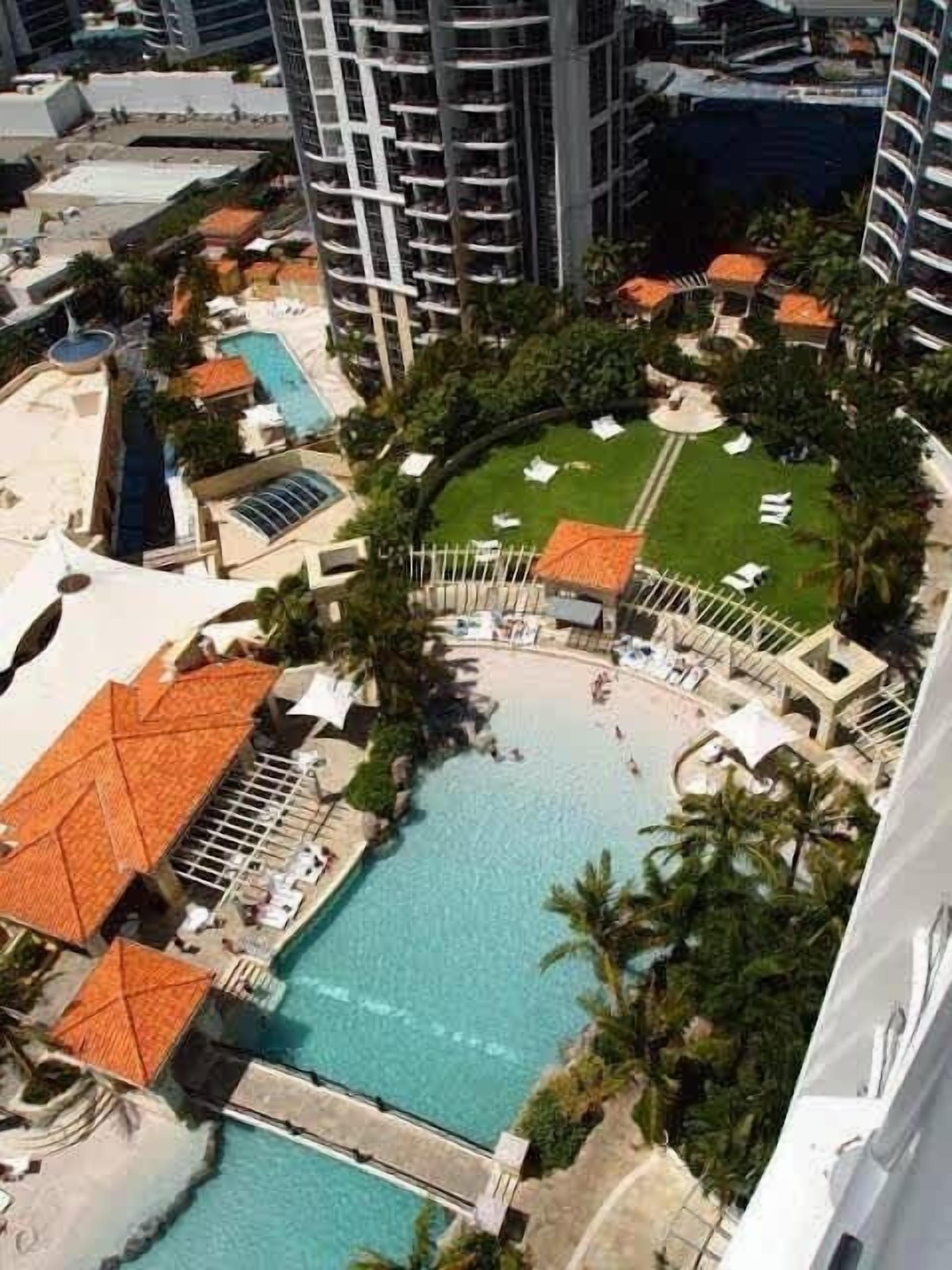 A high-rise hotel with a central swimming pool, multiple lounge areas, and a well-maintained garden.