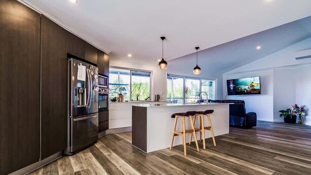 A modern kitchen with a large island, dark wood cabinetry, and a bar stool seating area. - Mudgeeraba family home with hot tub & garden (Mudgeeraba)