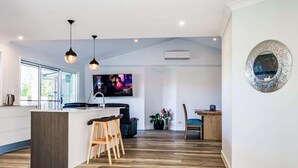 A modern kitchen with a central island, wooden bar stools, pendant lighting, and a television mounted on the wall. - Mudgeeraba family home with hot tub & garden (Mudgeeraba)