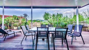An outdoor patio with a glass table and chairs, surrounded by lush greenery and a view of a distant landscape. - Mudgeeraba family home with hot tub & garden (Mudgeeraba)
