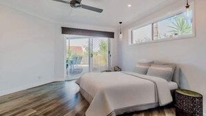 A bedroom with a bed, a ceiling fan, a window, and a door leading to a balcony. - Mudgeeraba family home with hot tub & garden (Mudgeeraba)