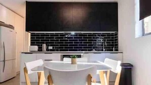 A modern kitchen with a black backsplash, white cabinets, and a round dining table with wooden chairs.