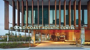 The exterior of the Gold Coast Aquatic Centre with a modern architectural design, featuring vertical wooden slats and large glass windows. - Vintage Coastal House | Fenced Pet-Friendly Yard (Labrador)