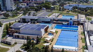 An aerial view of a building with a swimming pool, solar panels, and a parking lot. - Vintage Coastal House | Fenced Pet-Friendly Yard (Labrador)