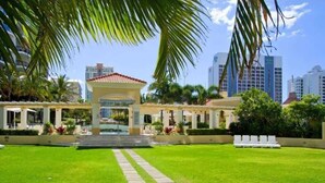 Um pátio com um gazebo central, rodeado por um gramado bem cuidado e palmeiras.