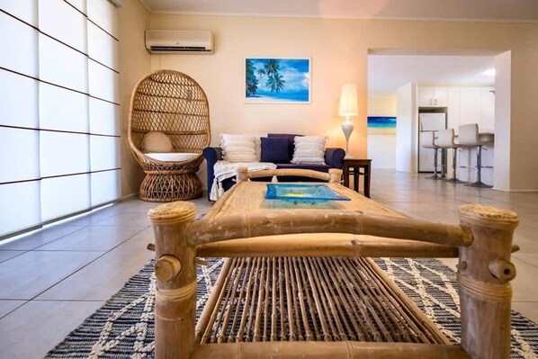 A room with a bamboo bed, wicker chair, and a view of the kitchen area.