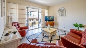 Un salon avec un canapé en cuir rouge, une table basse et un téléviseur. Il y a une fenêtre donnant sur l’extérieur.