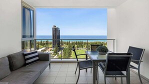 Een balkon met uitzicht op de oceaan en een hoog gebouw, ingericht met een bank, stoelen en een tafel.