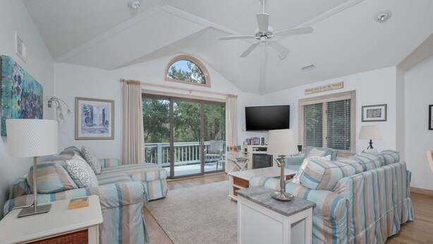 A spacious living room with a ceiling fan, a large TV, and a balcony with a view of trees. - 4603-Yellow Brick Road - Southern Shores Escape w/ Pool & Hot Tub (Southern Shores)