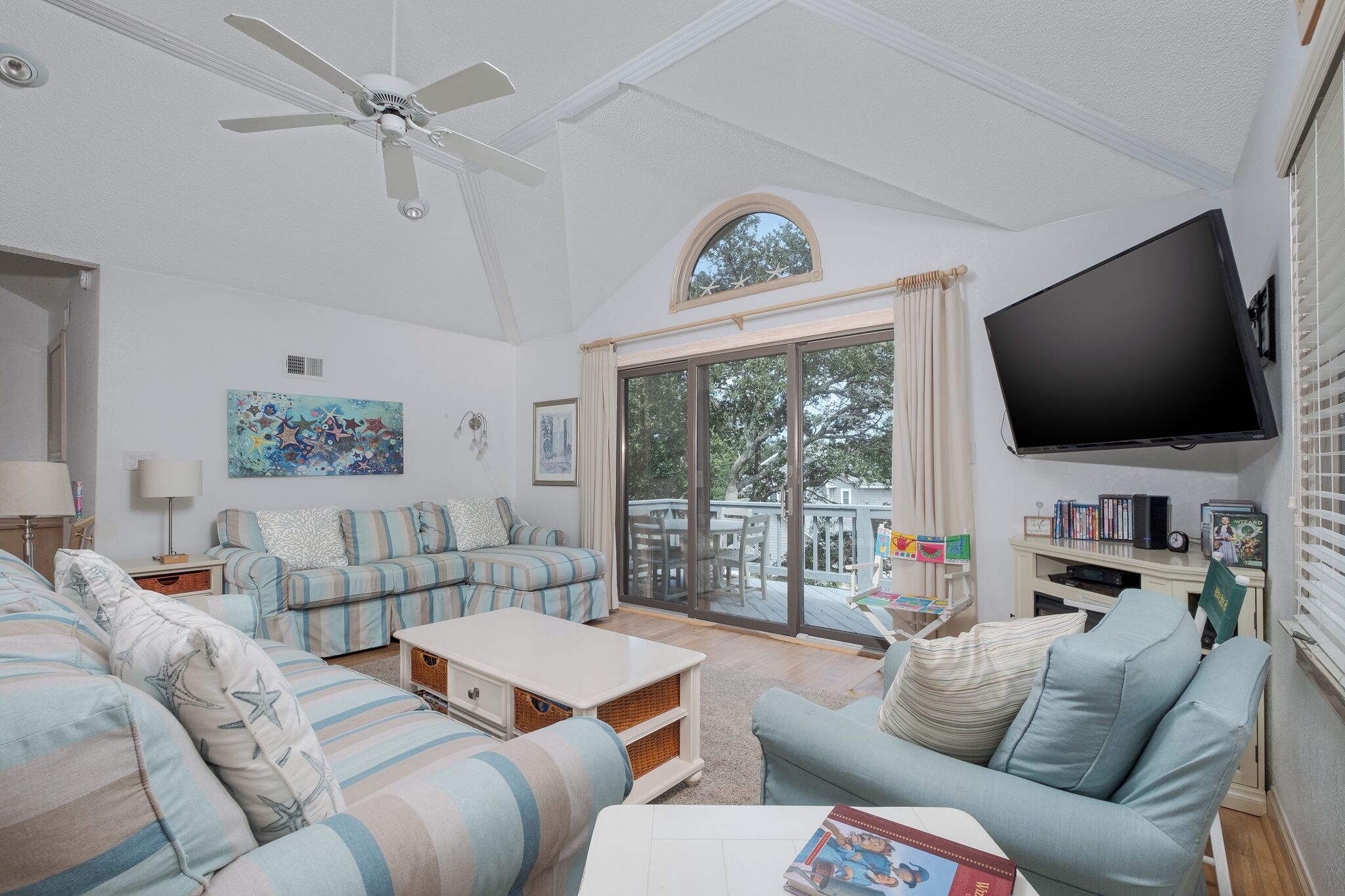 A spacious living room with a ceiling fan, a large TV, and a sliding glass door leading to a deck.