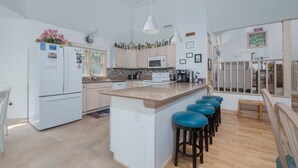 A spacious kitchen with a central island, bar stools, and a dining area. - 4603-Yellow Brick Road - Southern Shores Escape w/ Pool & Hot Tub (Southern Shores)