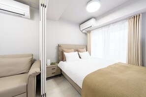 Una habitación de hotel moderna con cama, sofá, mesita de noche y aire acondicionado.