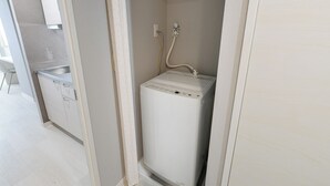 Ein kompakter, weißer Durchlauferhitzer an der Wand in einem schmalen Flur mit einem weißen Waschbecken und Schränken.