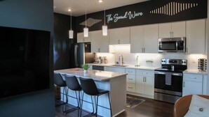 A modern kitchen with a central island, white cabinetry, stainless steel appliances, and pendant lighting. - The Sound Wave Luxury Condo Near Vanderbilt on Music Row, Just Minutes to Broadway (Nashville)