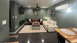 A modern living room with a dark green wall, a brown leather sofa, a white sofa, a wooden coffee table, and a TV mounted on the wall. - Charming Eastham Guesthouse (Charlottesville)
