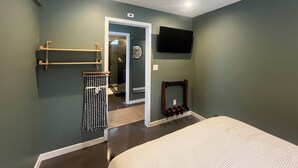 A bedroom with a bed, a ceiling fan, a TV, a coat rack, and a bathroom with a shower and toilet. - Charming Eastham Guesthouse (Charlottesville)