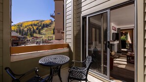 A balcony with a table and chairs, a sliding glass door, and a view of a village center with buildings and a mountain. - Kendall 231 - Managed by Purgatory Resort (Durango)