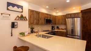 A modern kitchen with wooden cabinets, stainless steel appliances, a white countertop, and a built-in microwave. - Kendall 231 - Managed by Purgatory Resort (Durango)